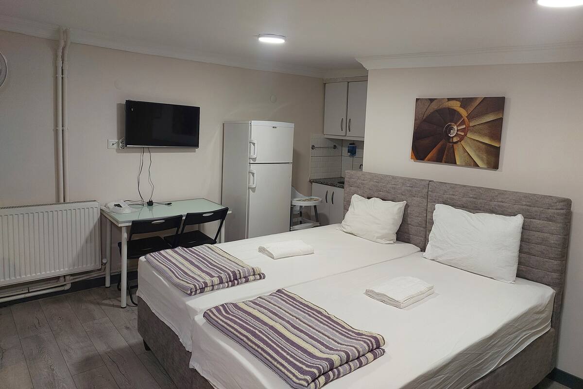 Habitación de hotel con cama, escritorio, refrigerador, televisor y un cuadro en la pared.
