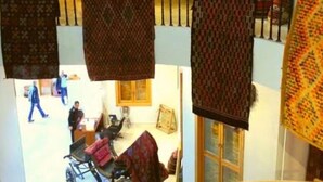 Ein mehrgeschossiges Interieur mit hängenden Textilien, einer Treppe und einem Raum mit Rollstuhl.