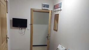 Ein Zimmer mit Holzboden, einem weißen Tisch mit Stühlen, einem an der Wand befestigten Fernseher und einer Tür zu einem weiteren Raum.