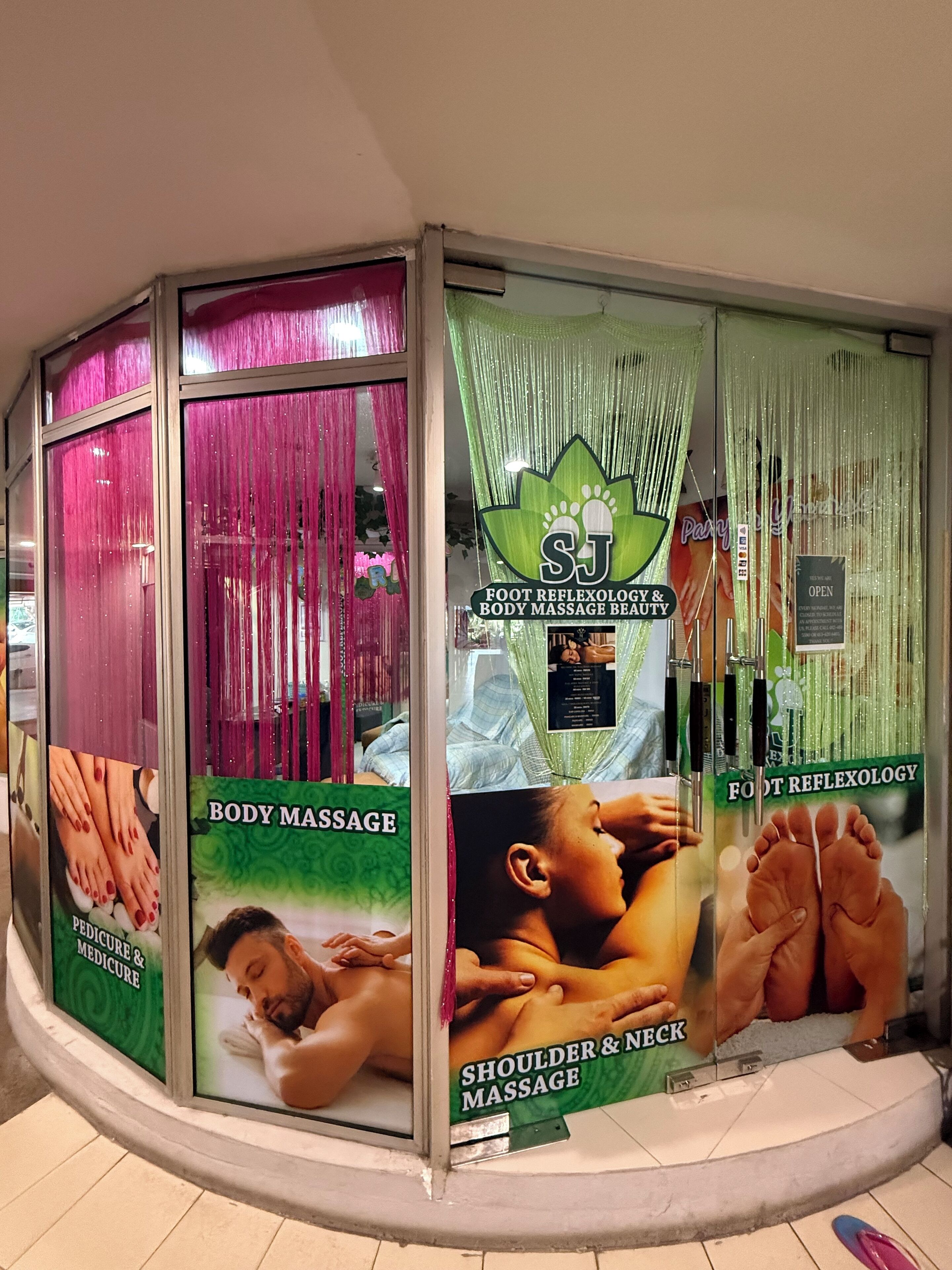 Een massagesalon met posters die diensten aanprijzen zoals lichaamsmassage, pedicure en voetreflexologie.