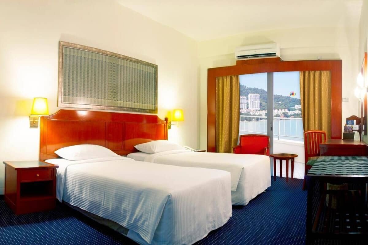 Ein Hotelzimmer mit zwei Betten, einem Schreibtisch, einem Stuhl und Blick auf eine Stadtlandschaft durch ein großes Fenster.