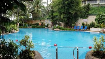 A swimming pool with blue water, surrounded by rocks and plants. There are lounge chairs and a person near the pool.