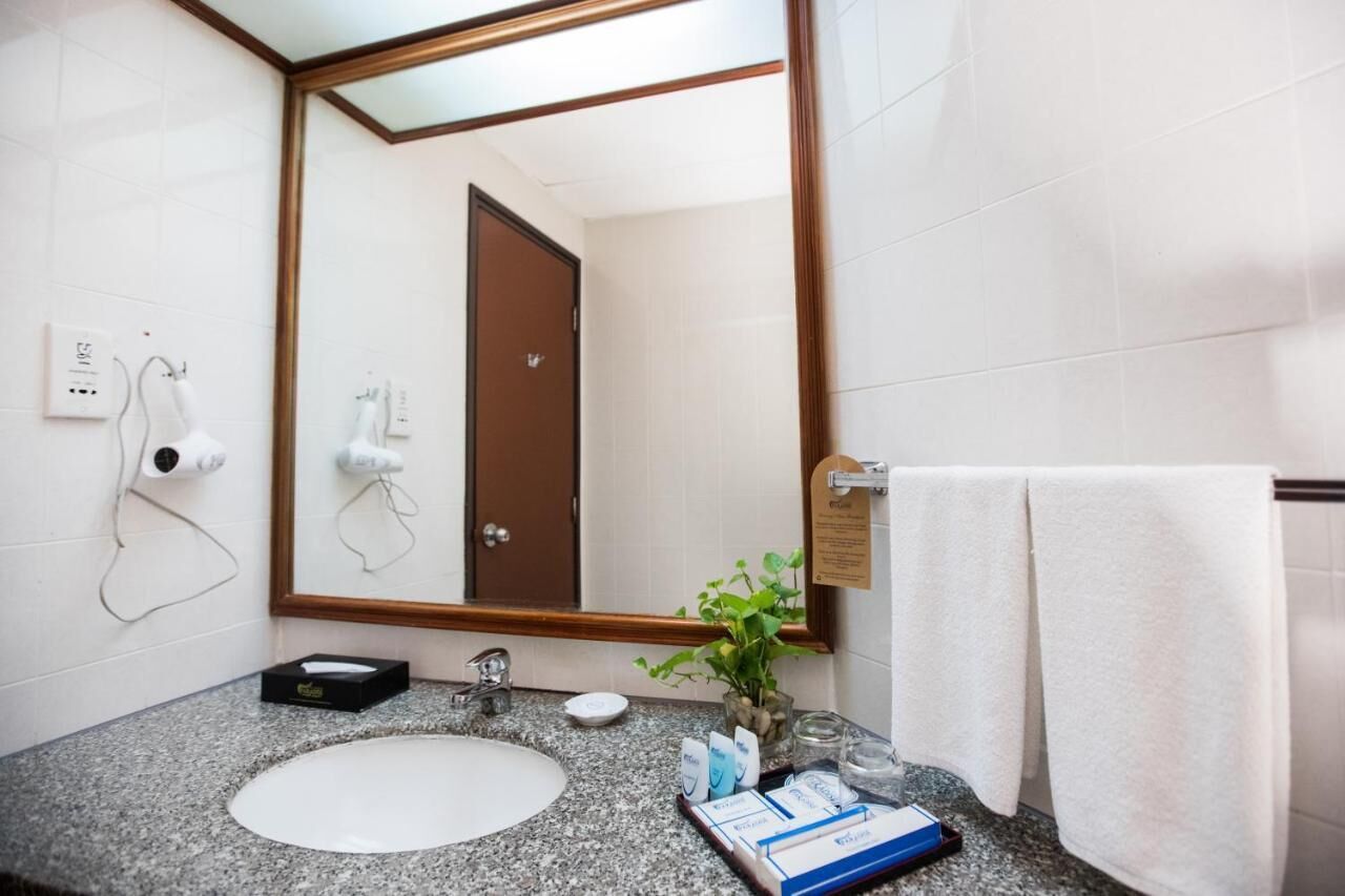 A hotel bathroom with a large mirror, a sink, a towel rack, a hairdryer, and toiletries on the counter.