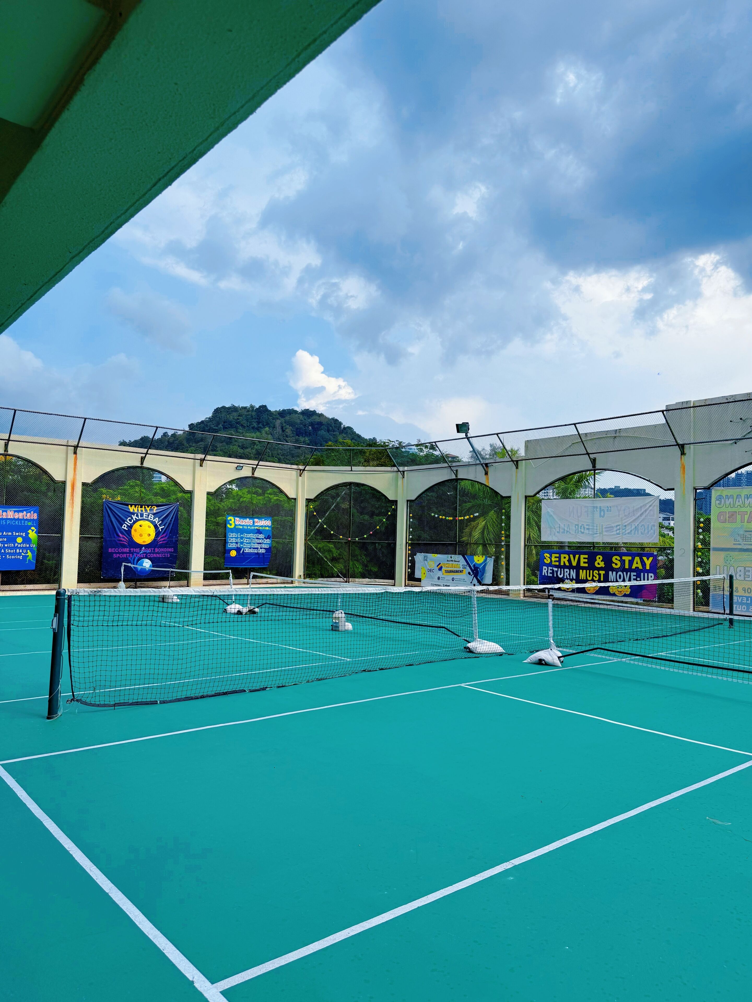 Pistes de tenis amb una xarxa, envoltades per una zona coberta amb seients, pancartes i senyalització.
