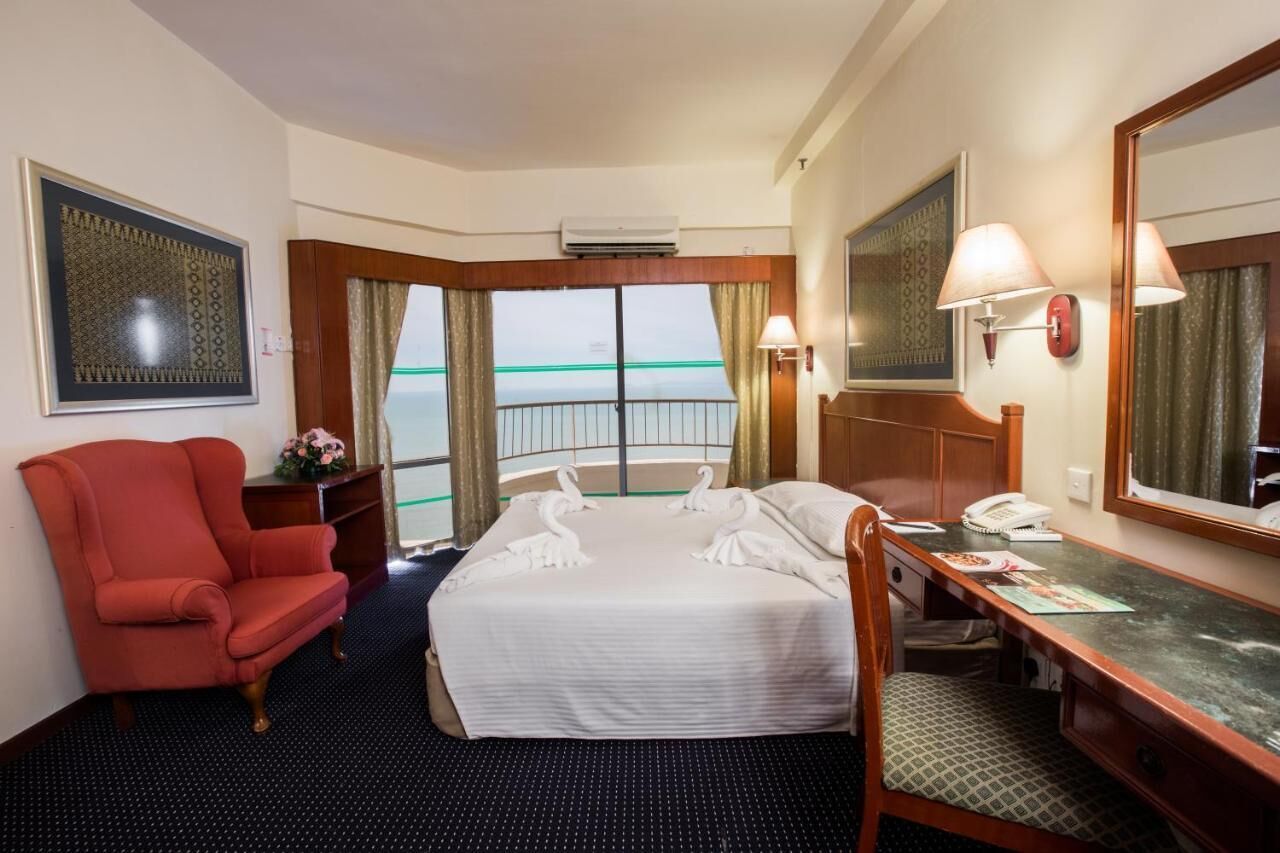 A hotel room with a bed, a desk, a chair, a large mirror, and a view of the sea.