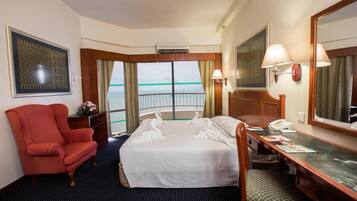 A hotel room with a bed, a desk, a chair, a large mirror, and a view of the sea.