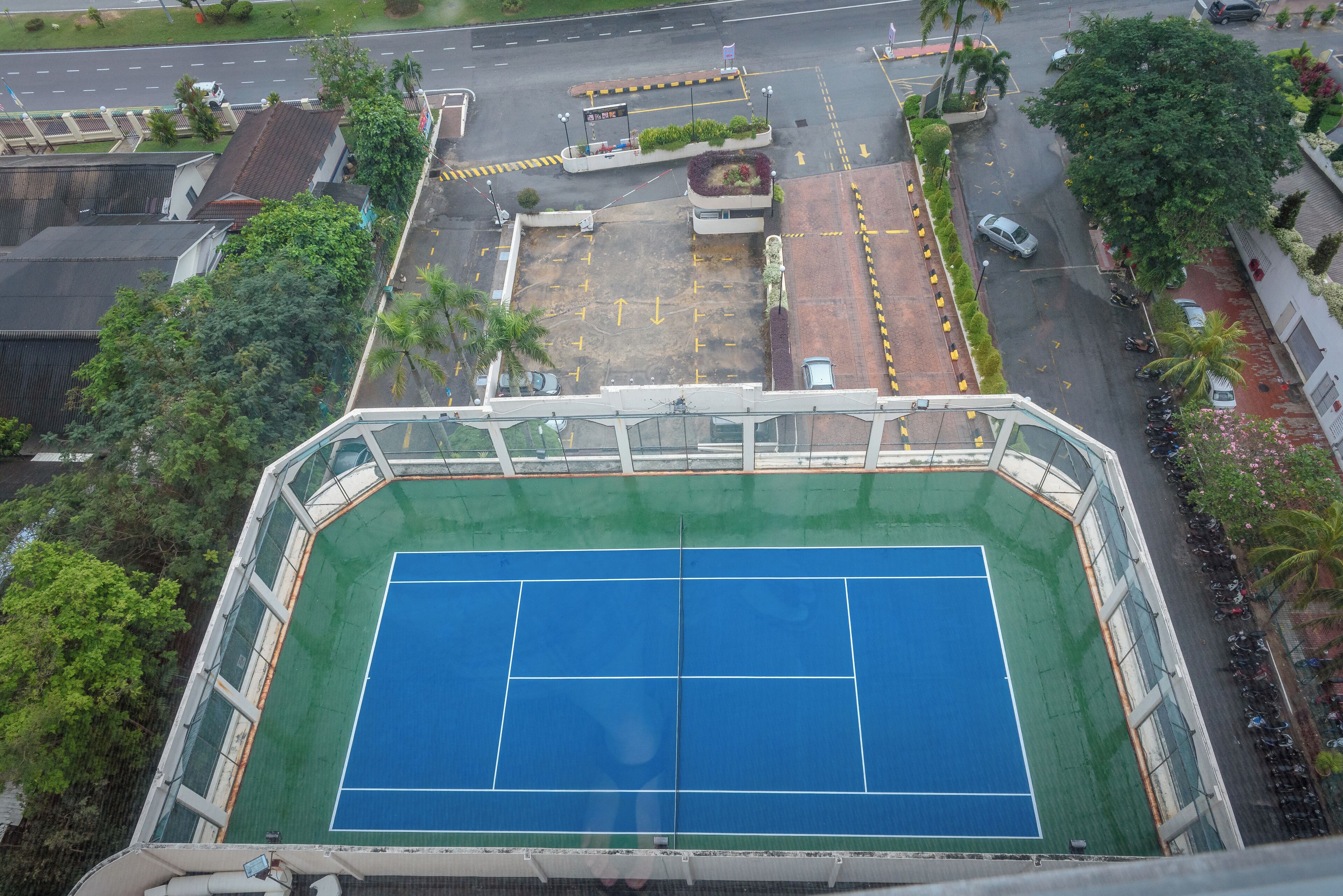 An aerial view of a tennis court surrounded by buildings and a parking area.