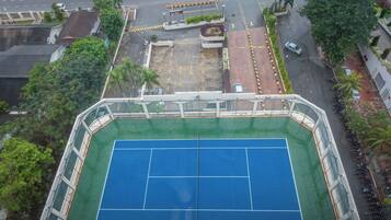 An aerial view of a tennis court surrounded by buildings and a parking area.