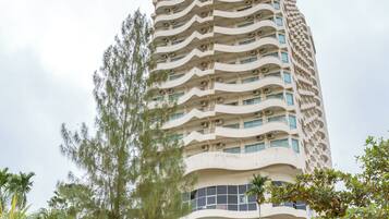 A tall, multi-story building with a unique wavy facade, surrounded by lush greenery and palm trees.