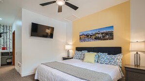 A bedroom with a bed, two bedside tables with lamps, a ceiling fan, a TV on the wall, and a painting above the bed. - King Room, Economy, Boutique Mtn Motel Idaho Springs (Idaho Springs)