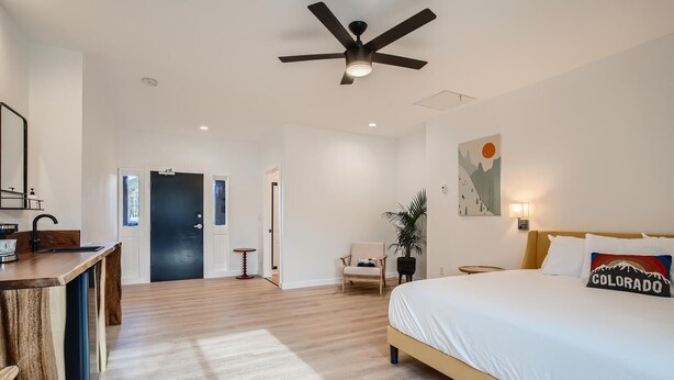 A modern hotel room with a wooden floor, a bed with a 'Colorado' pillow, a desk with a mirror, a chair, and a ceiling fan. - King Room, A/C, Boutique Mtn Motel Idaho Springs (Idaho Springs)