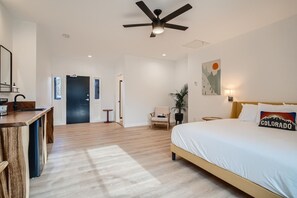 Une chambre d’hôtel moderne avec un plancher en bois, un lit agrémenté d’un oreiller « Colorado », un bureau avec un miroir, une chaise et un ventilateur de plafond.