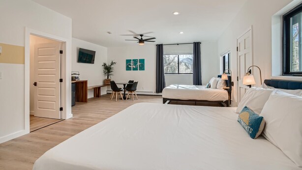 A modern hotel room with a large bed, a desk, and a chair. There is a ceiling fan and a window with curtains. - 2x King Room, A/C, Balcony, Mtn Boutique Motel (Idaho Springs)