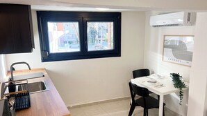 Cocina compacta con ventana, una mesa de comedor con sillas, un lavamanos y un aire acondicionado de pared.