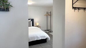 Un dormitorio con cama, mesita de noche, lámpara y un perchero.