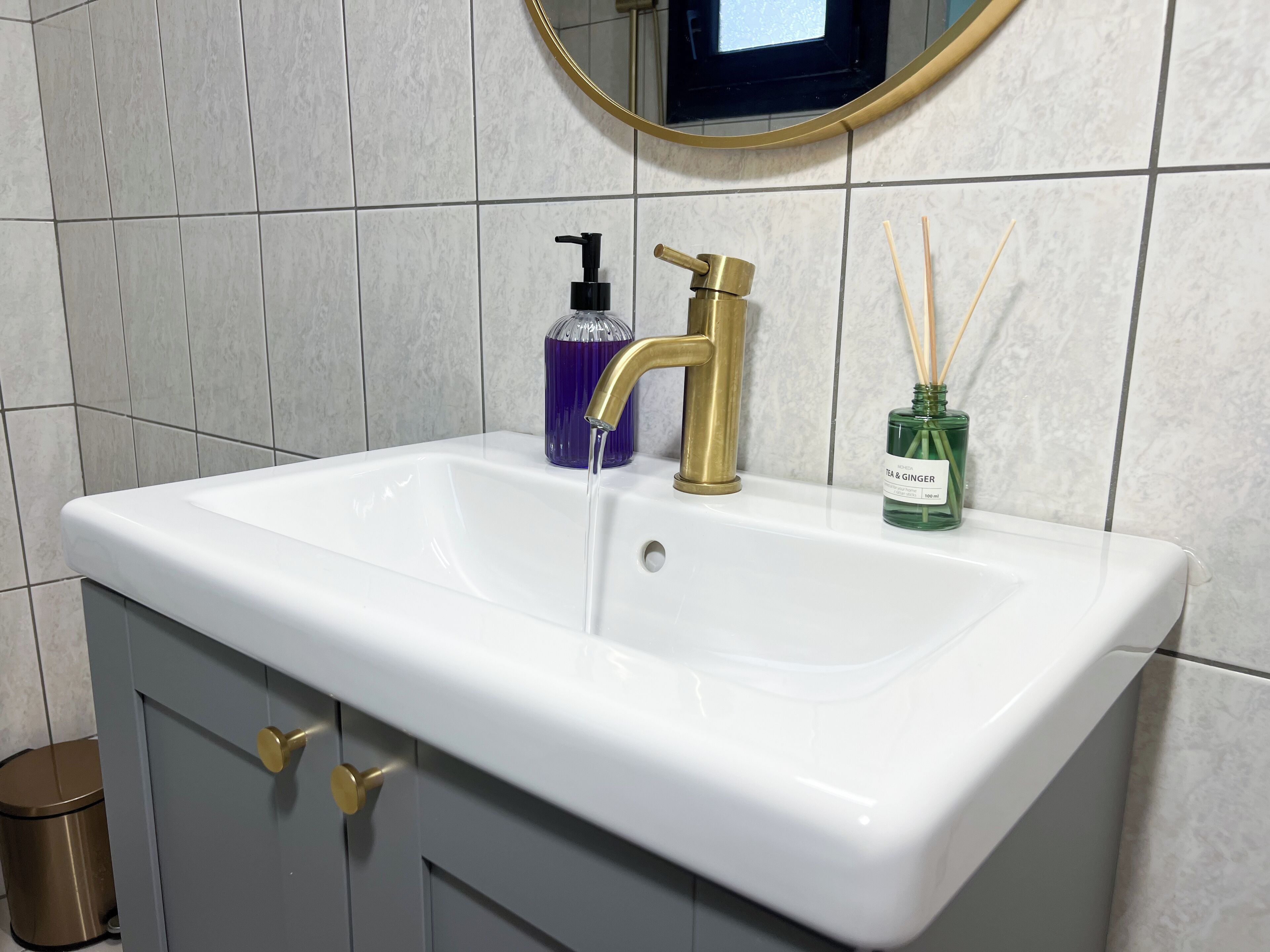 Un bagno con un lavandino bianco, un rubinetto dorato e un erogatore di sapone viola.