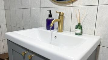 Un bagno con un lavandino bianco, un rubinetto dorato e un erogatore di sapone viola.