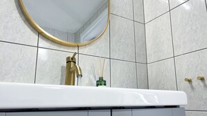 Un baño con lavamanos blanco, grifo dorado y espejo redondo con marco dorado.
