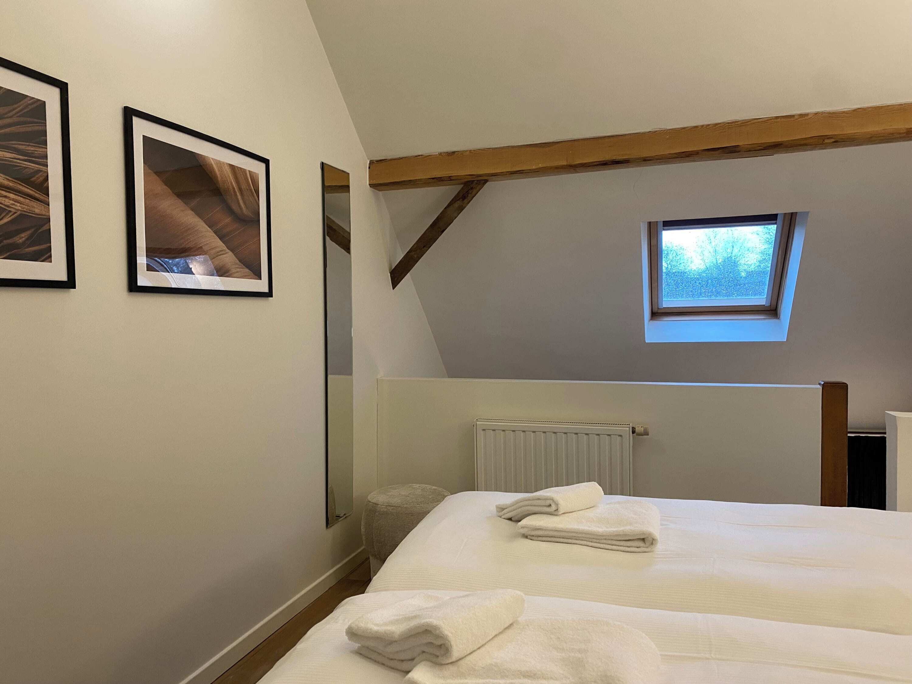 Una camera da letto con due letti, una finestra a lucernario, un termosifone e quadri appesi al muro.
