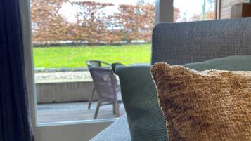 Uitzicht vanuit een kamer op een terras met een groen gazon en een stoel.