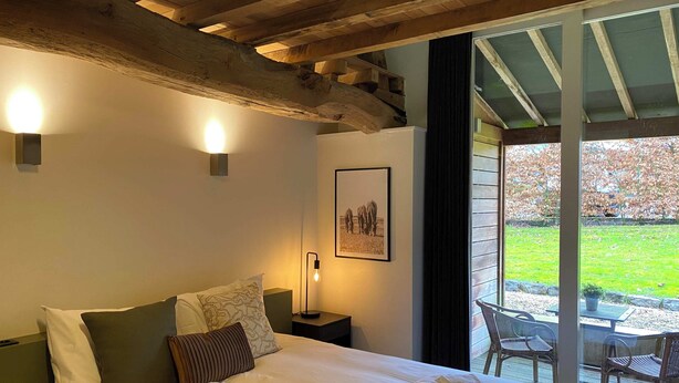 A hotel room with a large bed, two wall-mounted lights, a framed picture, and a view of the outdoors through a glass door. - A5. De Shetlander: deluxe room with terrace (Oudsbergen)