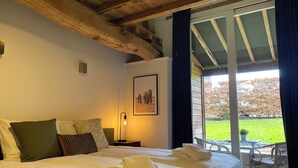 A hotel room with a large bed, a nightstand, a framed picture on the wall, and a view of the outdoors through a sliding door. - A5. De Shetlander: deluxe room with terrace (Oudsbergen)