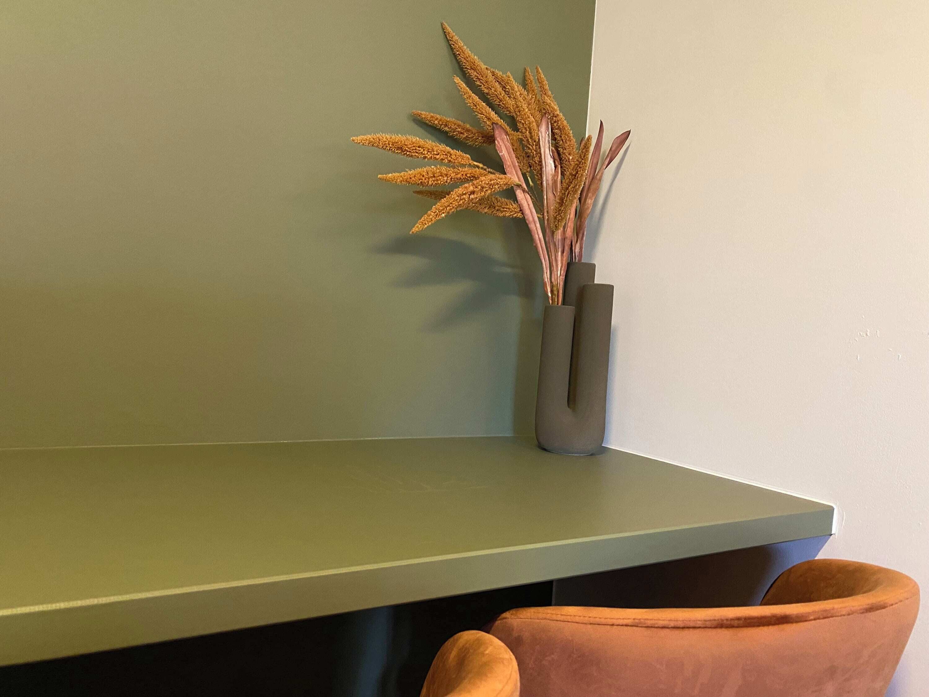 A corner of a room with a green wall, a dark brown chair, and a vase with dried plants.