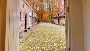 A cobblestone courtyard with brick buildings and autumn foliage. - A5. De Shetlander: deluxe room with terrace (Oudsbergen)