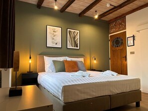 A neatly made bed with pillows and a folded towel, a bedside lamp, and framed artwork on the wall. - Deluxe room B1 (Oudsbergen)