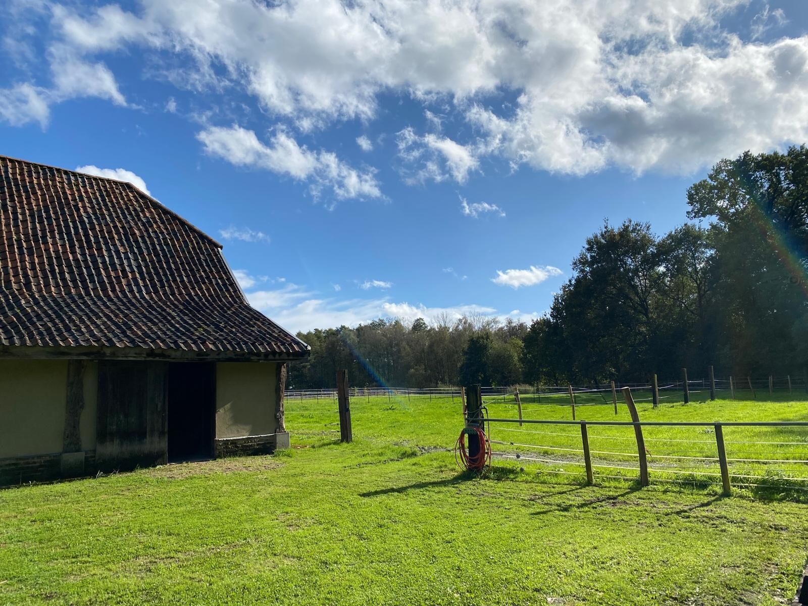 Ein ländliches Bauernhaus mit einem eingeschossigen Gebäude, einer eingezäunten Weide und blauem Himmel.
