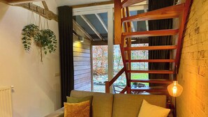 A cozy living room with a wooden staircase, a sofa with cushions, and a hanging plant.