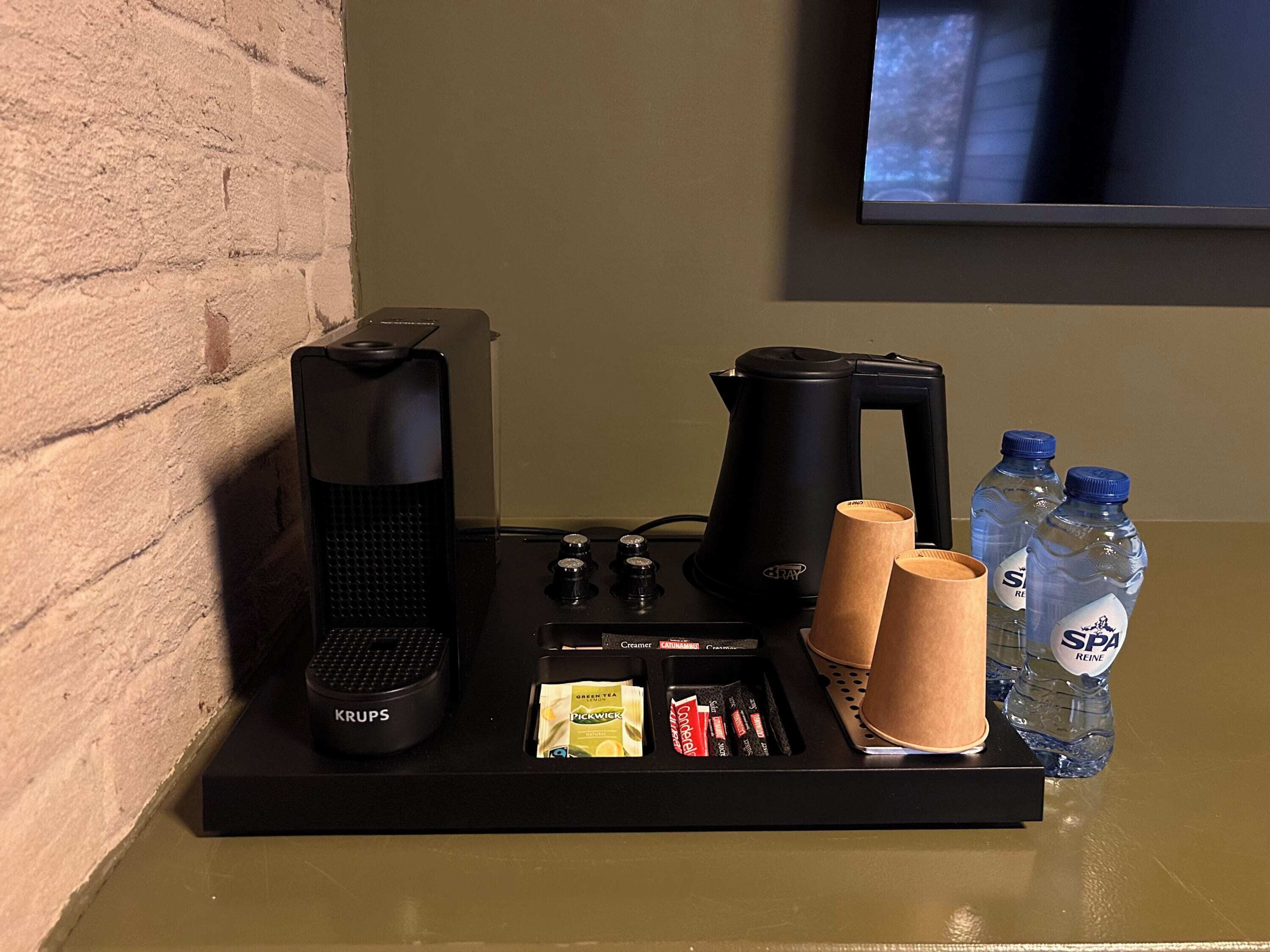 A coffee station with a Krups coffee maker, a coffee pot, and two water bottles labeled SPA.