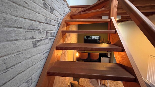 A wooden staircase with a brick wall on one side.