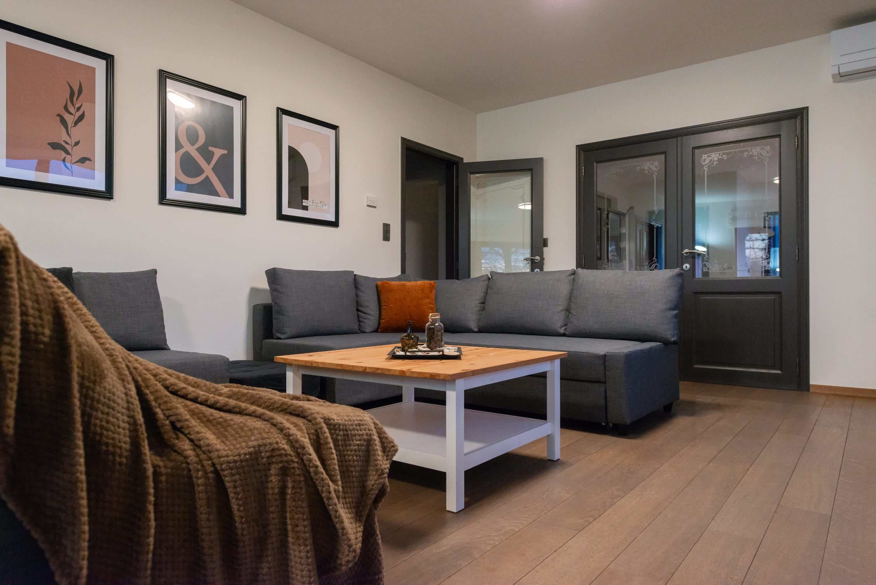 Una sala de estar moderna con un sofá gris, una mesa de centro de madera y una manta marrón en una silla.