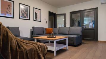 Una sala de estar moderna con un sofá gris, una mesa de centro de madera y una manta marrón en una silla.