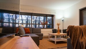 Een moderne woonkamer met een bank, salontafel en uitzicht op bomen door grote ramen.