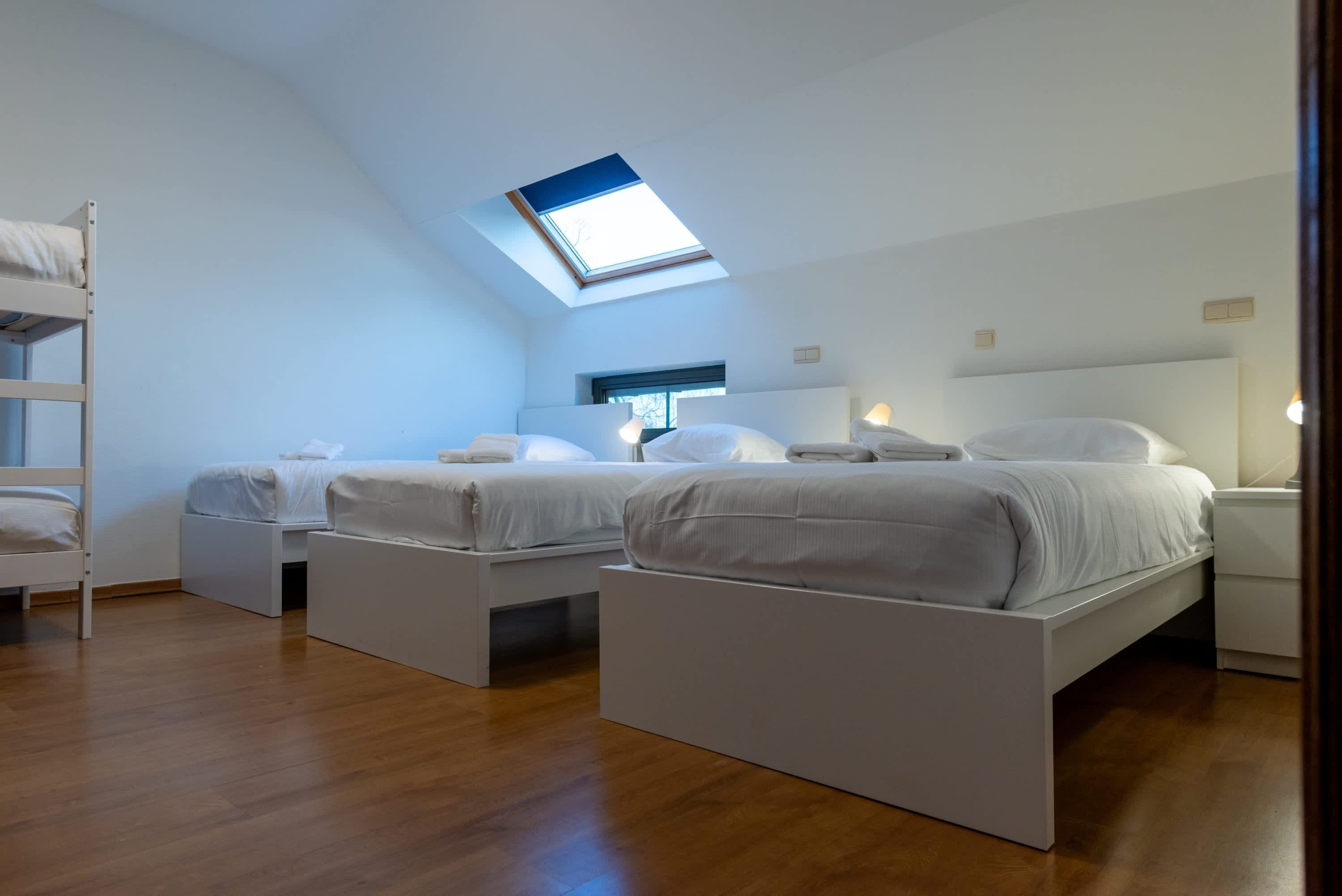 A modern bedroom with two beds, a skylight, and a wooden floor.