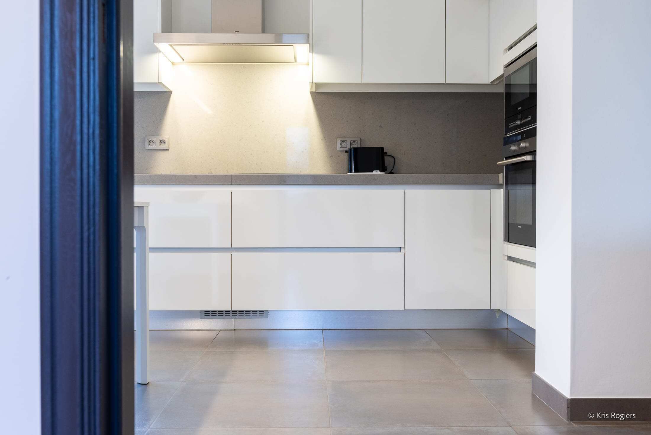 Una cocina moderna con gabinetes blancos, una campana extractora de acero inoxidable y un horno empotrado.