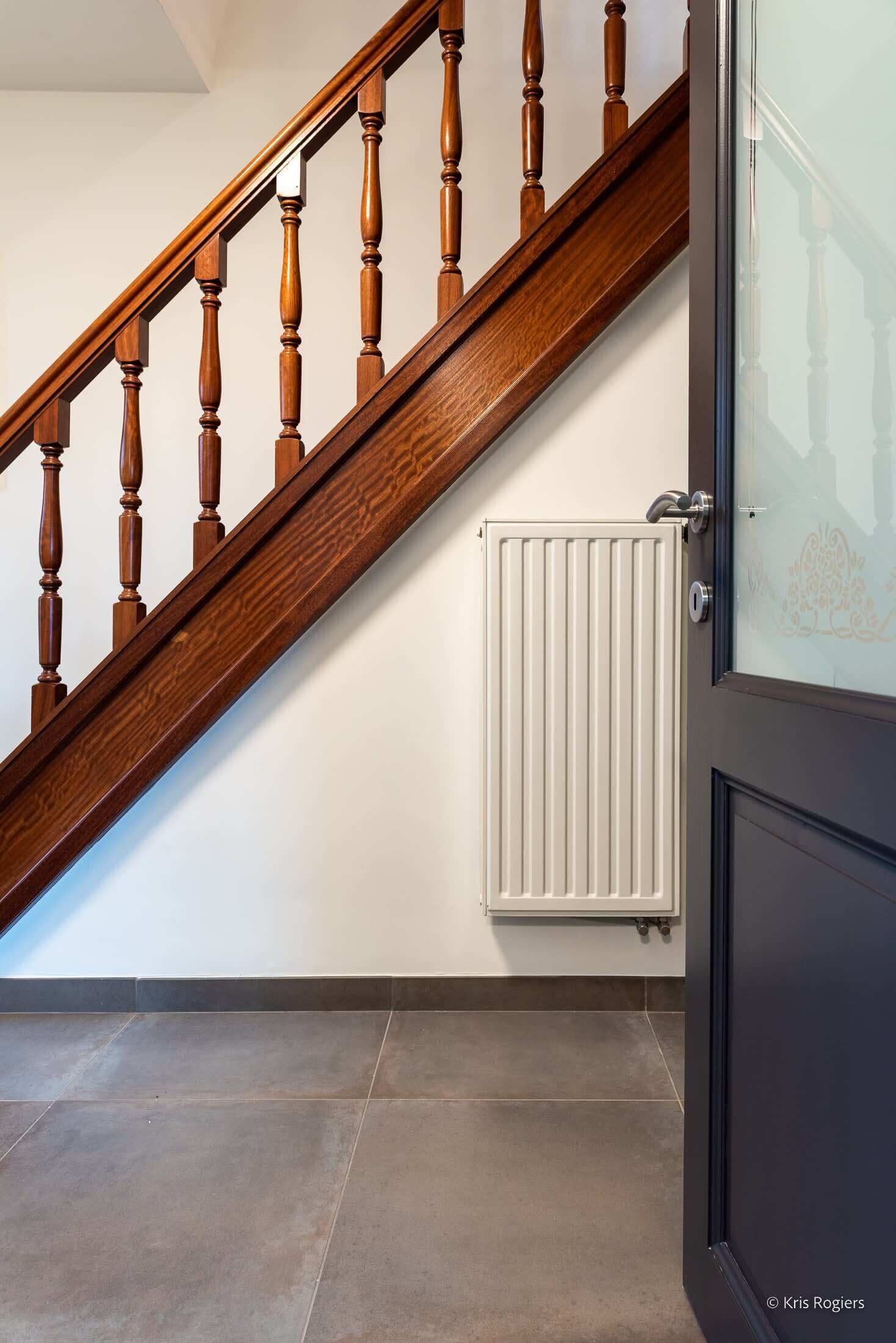 Una escalera de madera con un radiador blanco y una puerta con un panel de vidrio esmerilado.