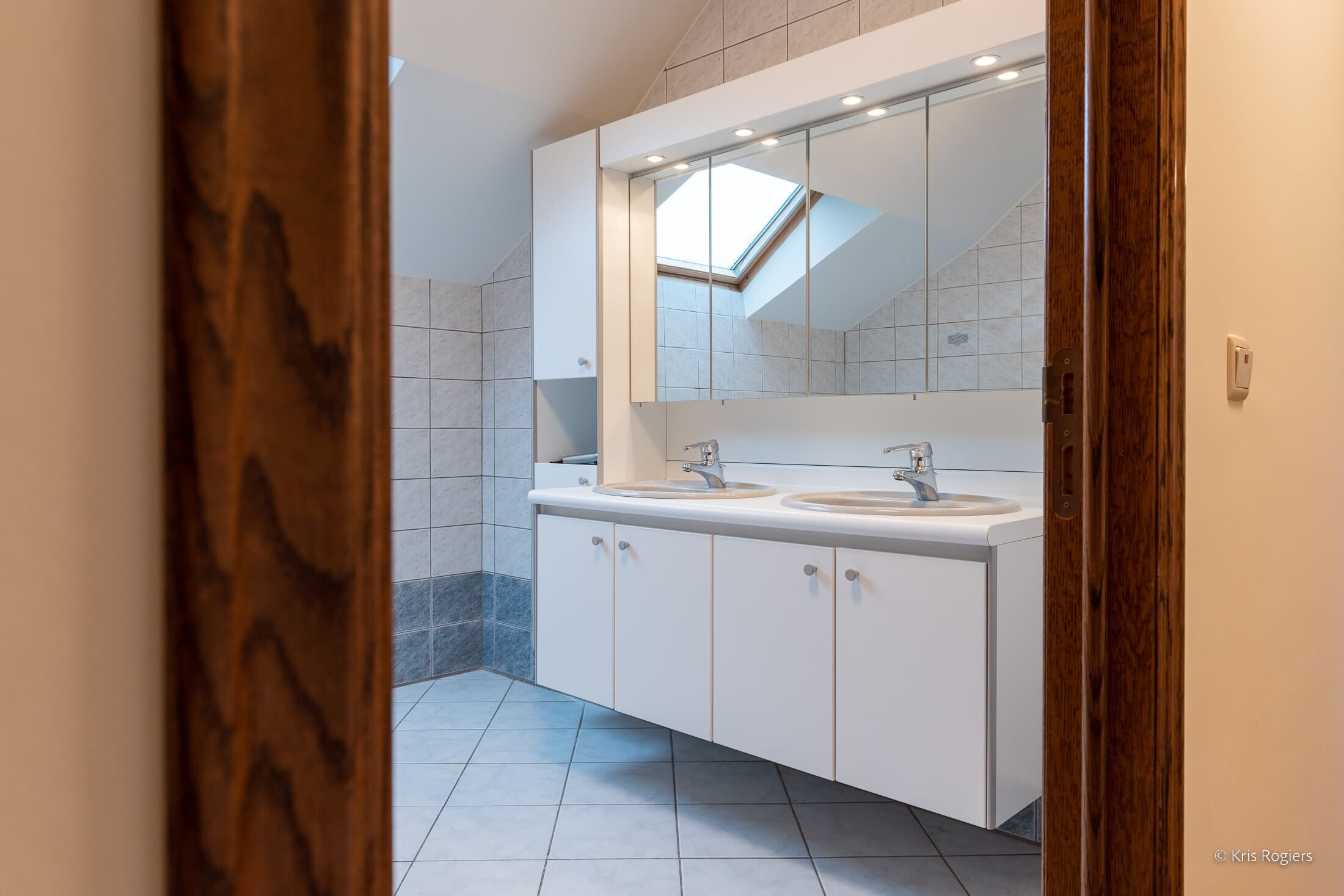 A modern bathroom with a skylight, two sinks, and a large mirror.