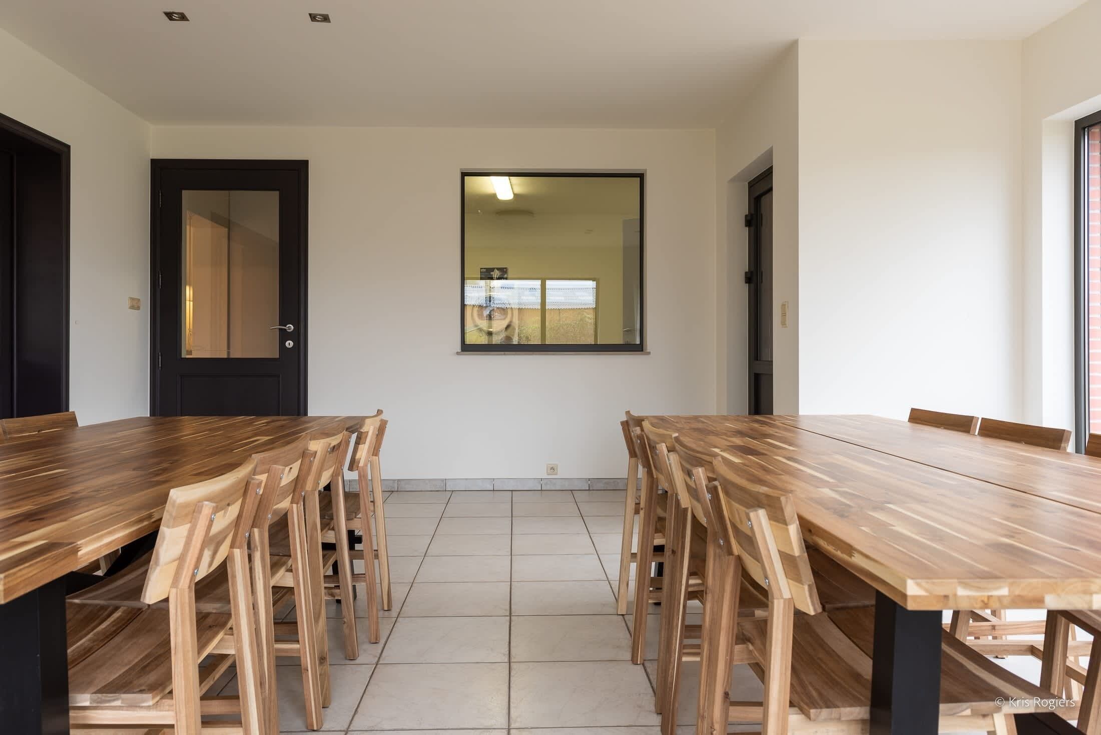 A dining area with a long wooden table and chairs, a black door, and a window with a view.