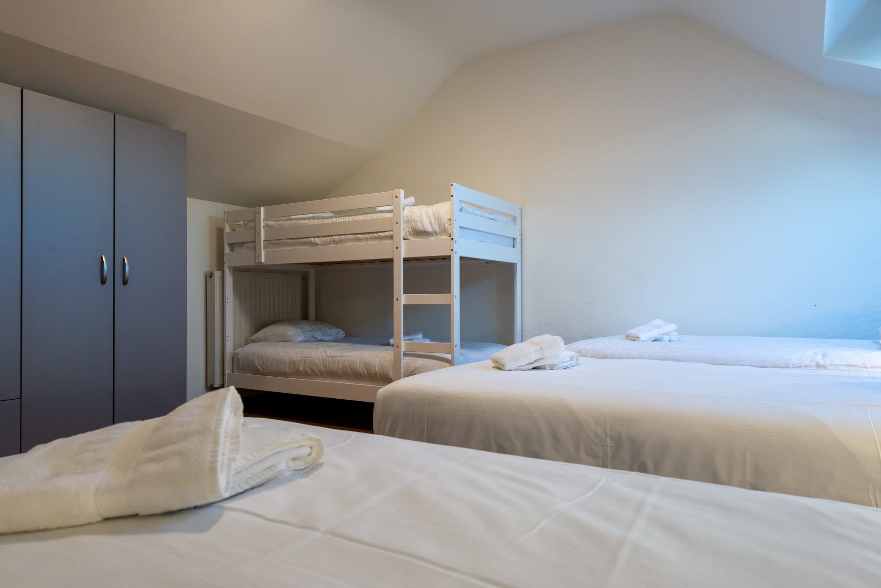 A dormitory room with bunk beds, a wardrobe, and neatly made beds.