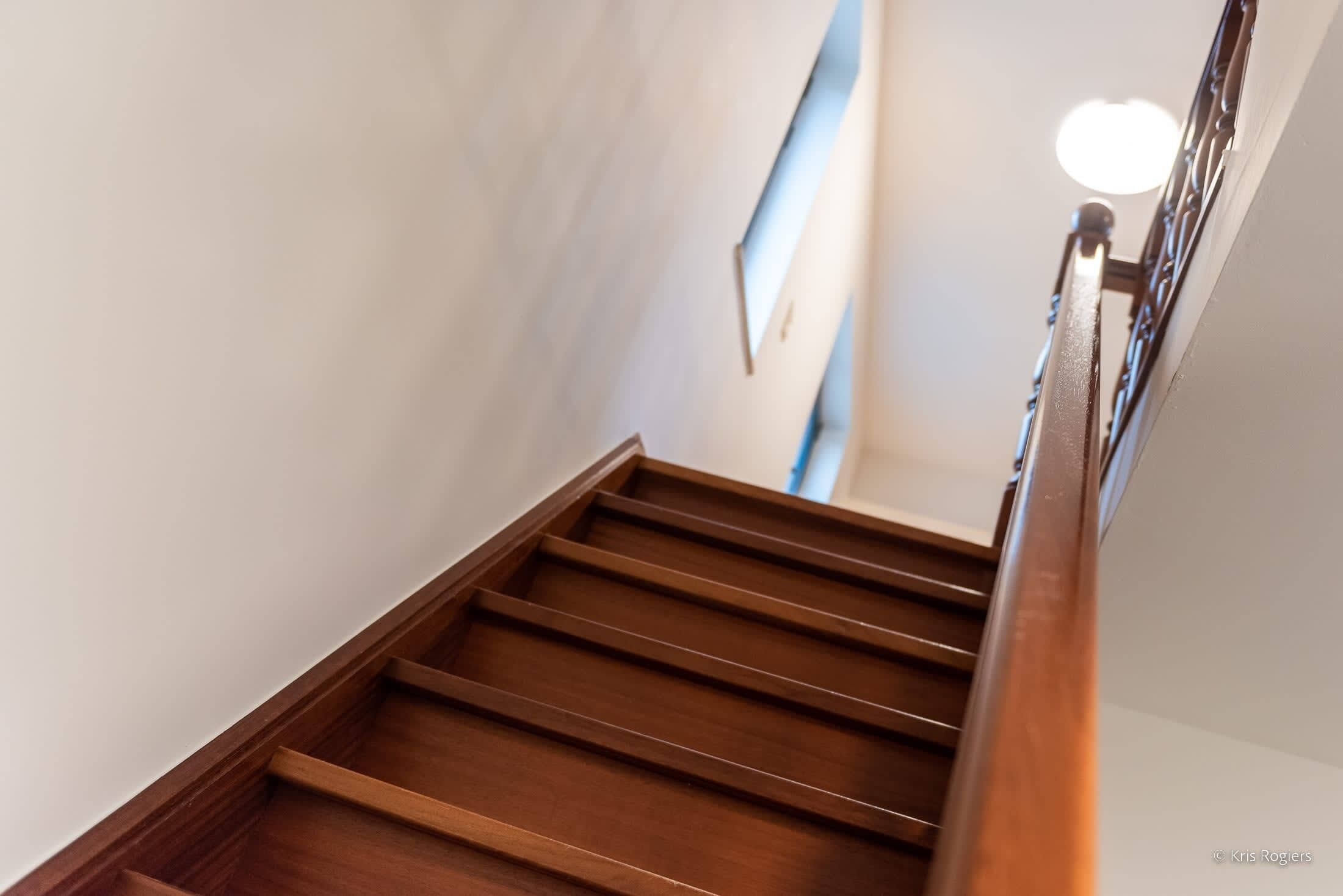 Una escalera de madera con barandilla y un aplique en la parte superior.