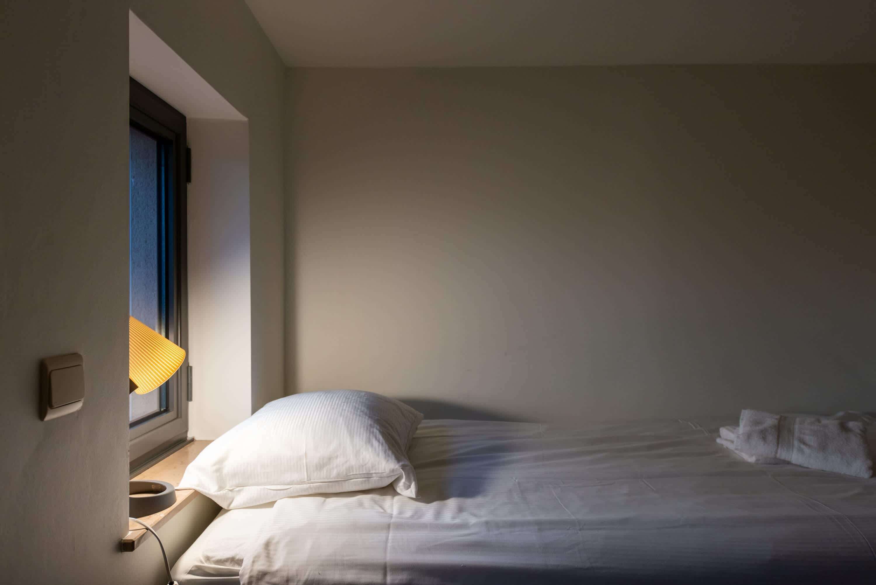A bedroom with a bed, a window with a lamp, and a wall-mounted switch.