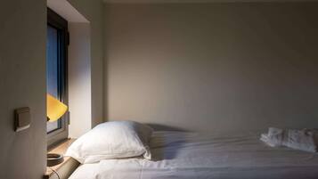 A bedroom with a bed, a window with a lamp, and a wall-mounted switch.