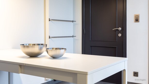 Een keuken met twee roestvrijstalen kommen op een wit aanrecht, een zwarte deur en een witte muur met een lichtschakelaar.
