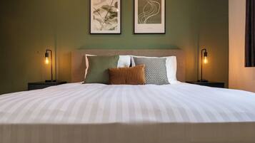 A neatly made bed with striped bedding, two framed artworks above it, and two bedside lamps on either side.