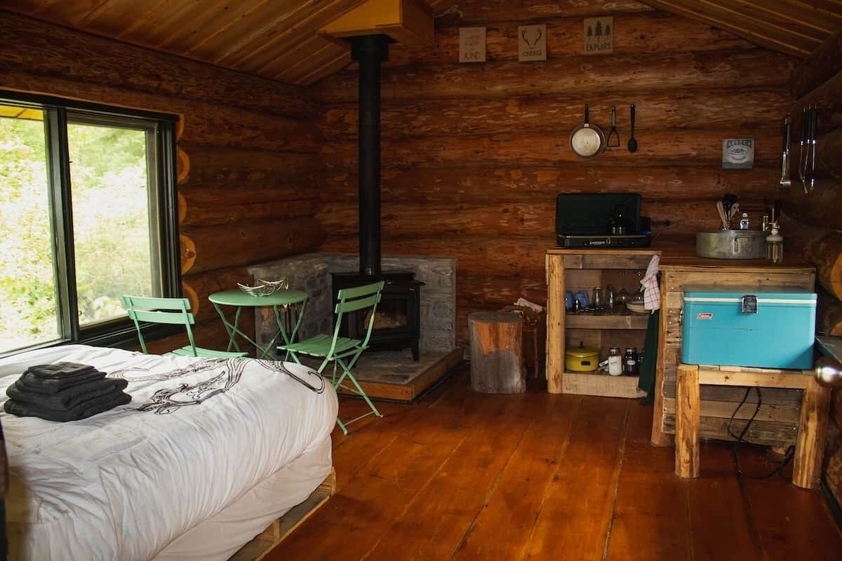 Une cabane confortable avec un lit, une cheminée, une petite table et une fenêtre.