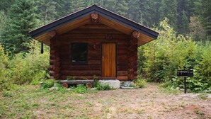A log cabin with a wooden door, a window, and a small porch. - Off-Grid WoodLog Cabin (Blaeberry)