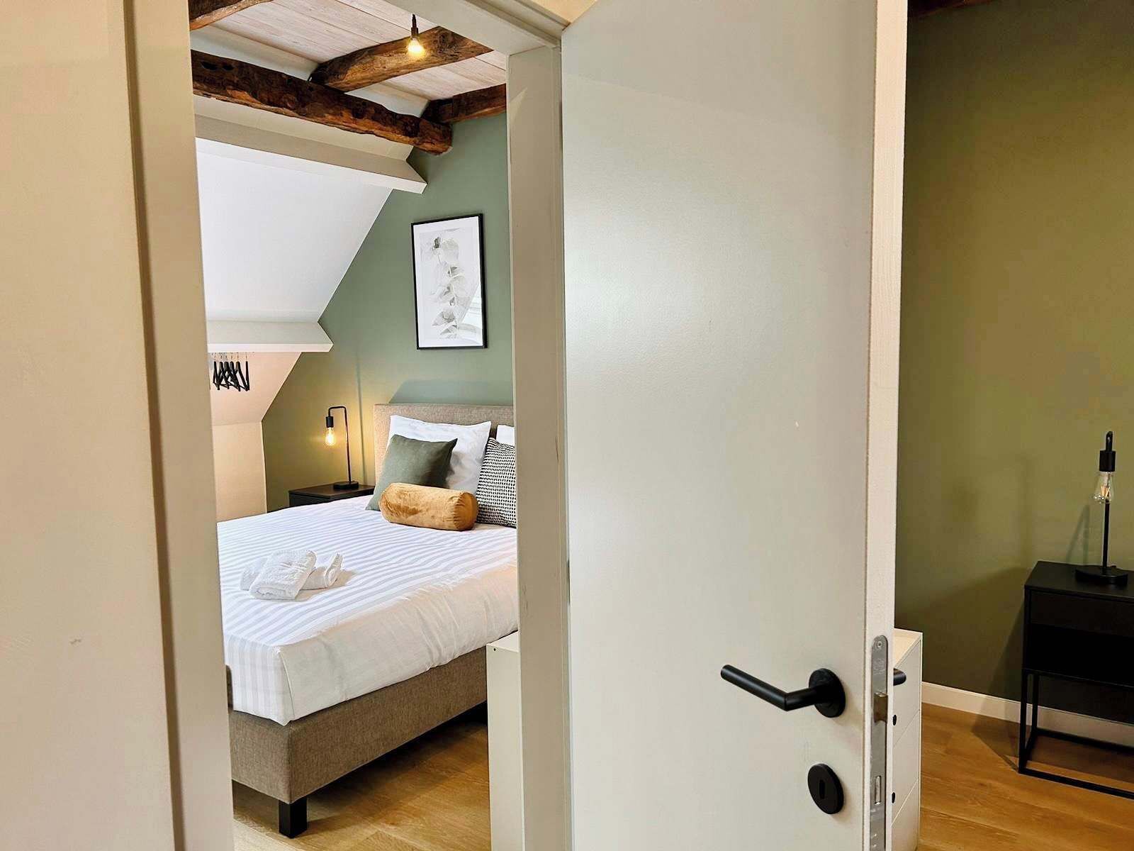 Una camera da letto con un letto, un comodino, una lampada a parete e una porta con maniglia.